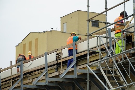 Robotnicy na rusztowaniu remontują budynek.